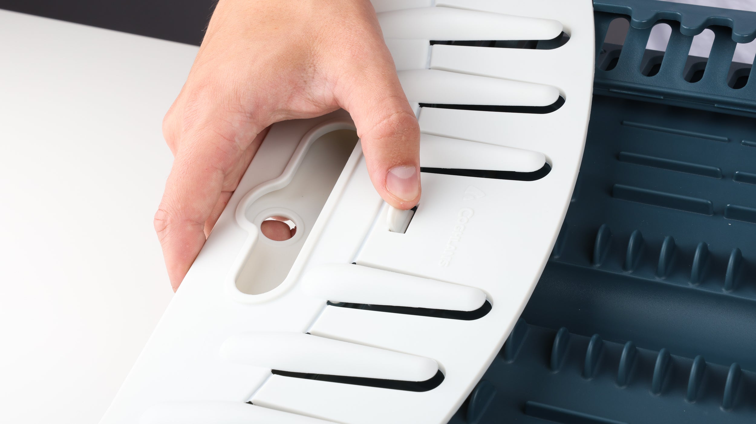 A thumb sliding a clip lock away from the center to open a Coghlan's Snapfold Dish Rack
